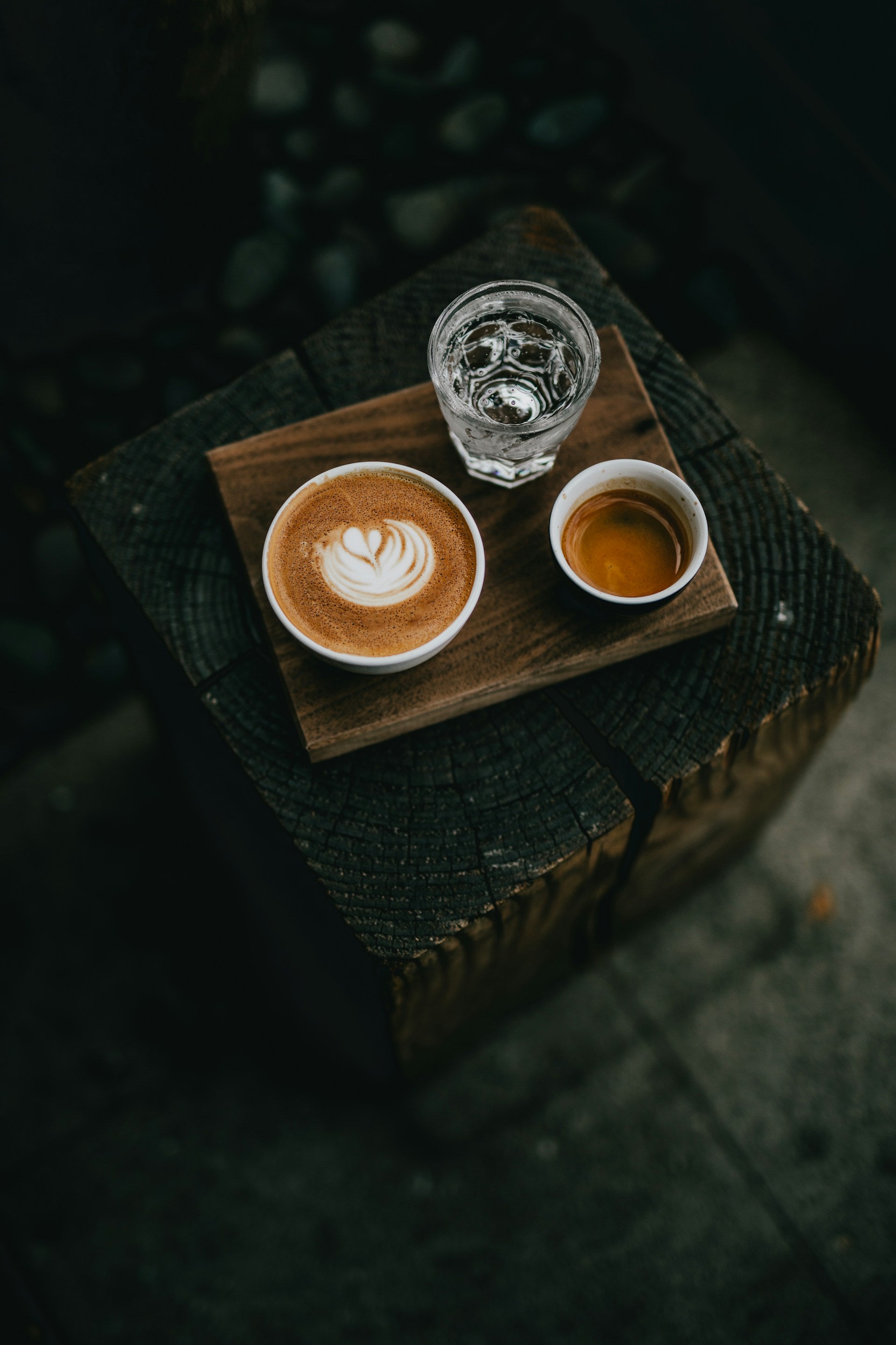 Noteworthy Selections Espresso Taster with a glass of water, espresso in a cup and a latte placed on a wooden serving board and table